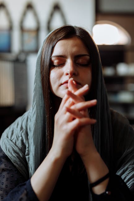A calm woman meditates with closed eyes in a tranquil, dimly lit environment.